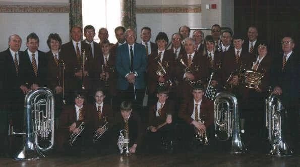 A colour group photograph of Emley band members of different ages, seated and standing with their brass instruments.