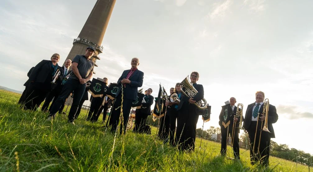 Members of Emley Brass Band performing beneath Emley Moor mast in 2026. Image via Huddersfield Hub.